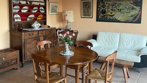 Ein Essbereich mit Holztisch und Stühlen, einer Blumenvase, einem Schrank mit Geschirr und einem Bild an der Wand.