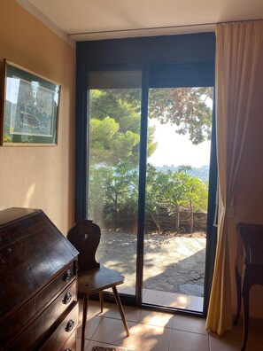 A room with a large sliding glass door, a wooden dresser, a chair, and a framed picture on the wall.