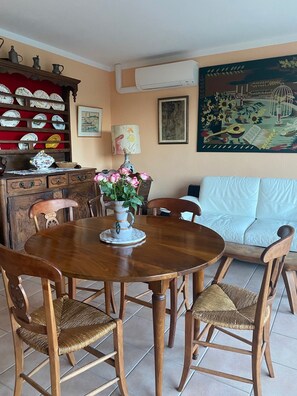 A dining area with a wooden table and chairs, a vase with flowers, a cabinet with dishes, and a sofa.