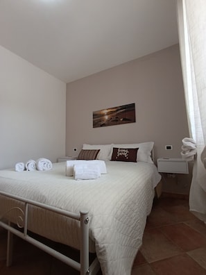 A neatly made bed with pillows, a bedside table, a wall-mounted artwork, and a curtain.