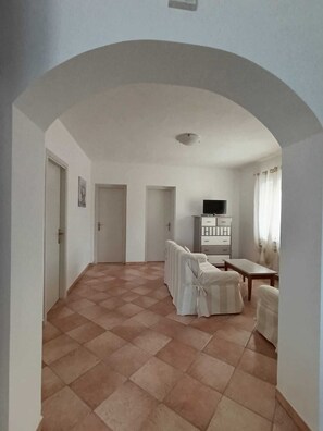 A spacious room with a tiled floor, a sofa, a TV, and a cabinet.