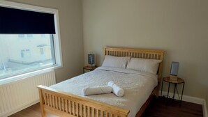Een slaapkamer met een houten bed, een nachtkastje, een lamp en een raam met jaloezieën.
