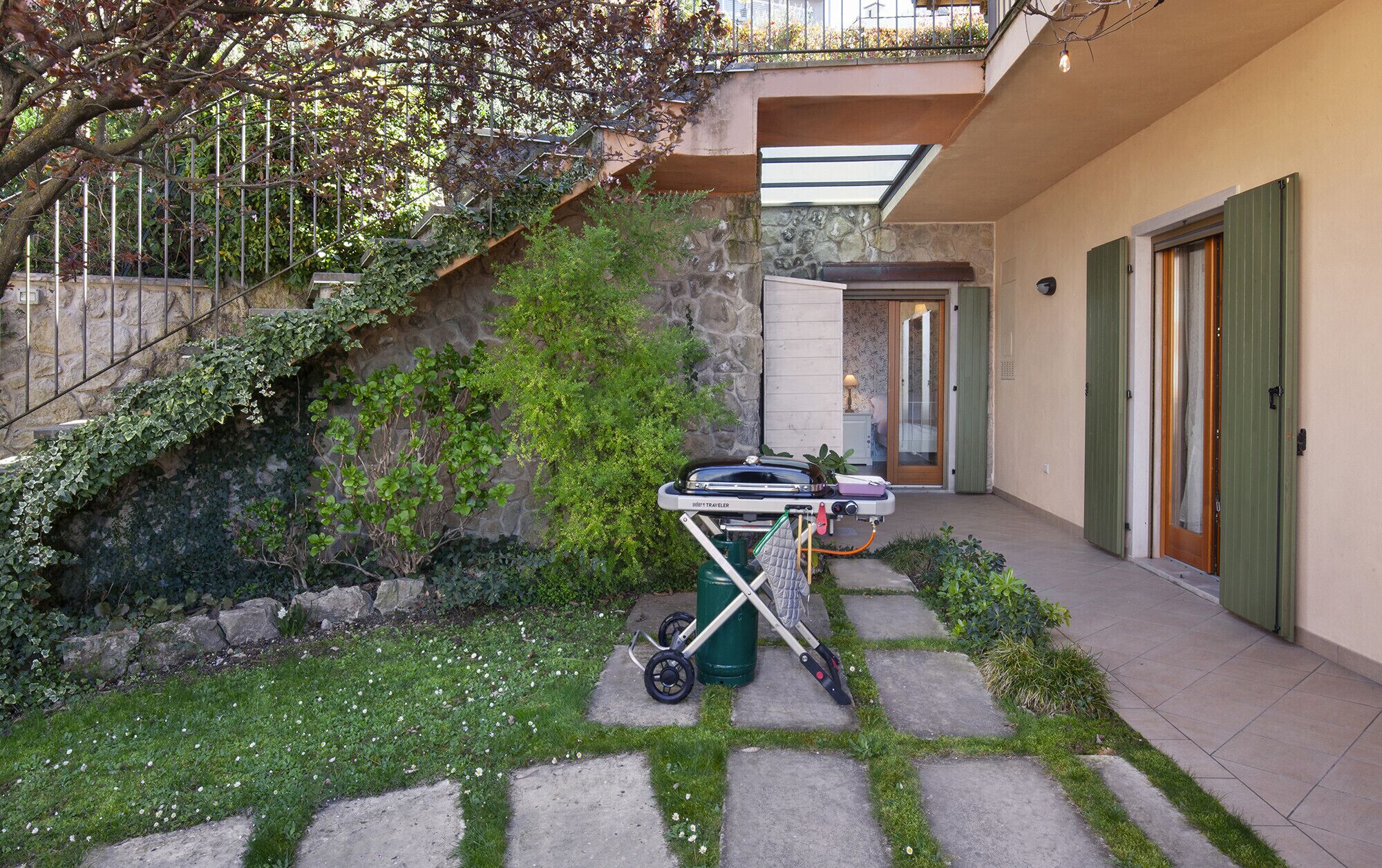 Um caminho de pedra leva a uma casa com porta verde, um pequeno jardim com flores brancas e um veículo estacionado.
