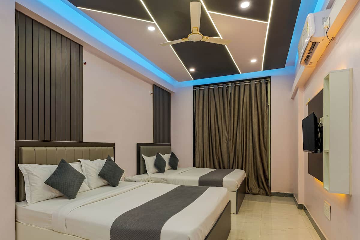 A modern hotel room with two beds, a ceiling fan, recessed lighting, and a flat-screen TV.