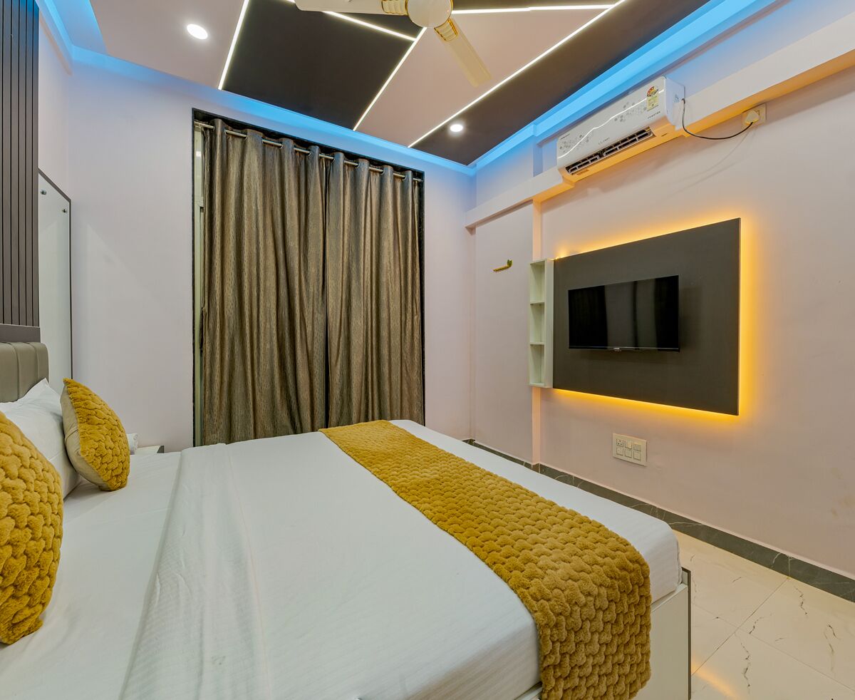A modern hotel room with a bed, curtains, a mounted TV, and an air conditioning unit.