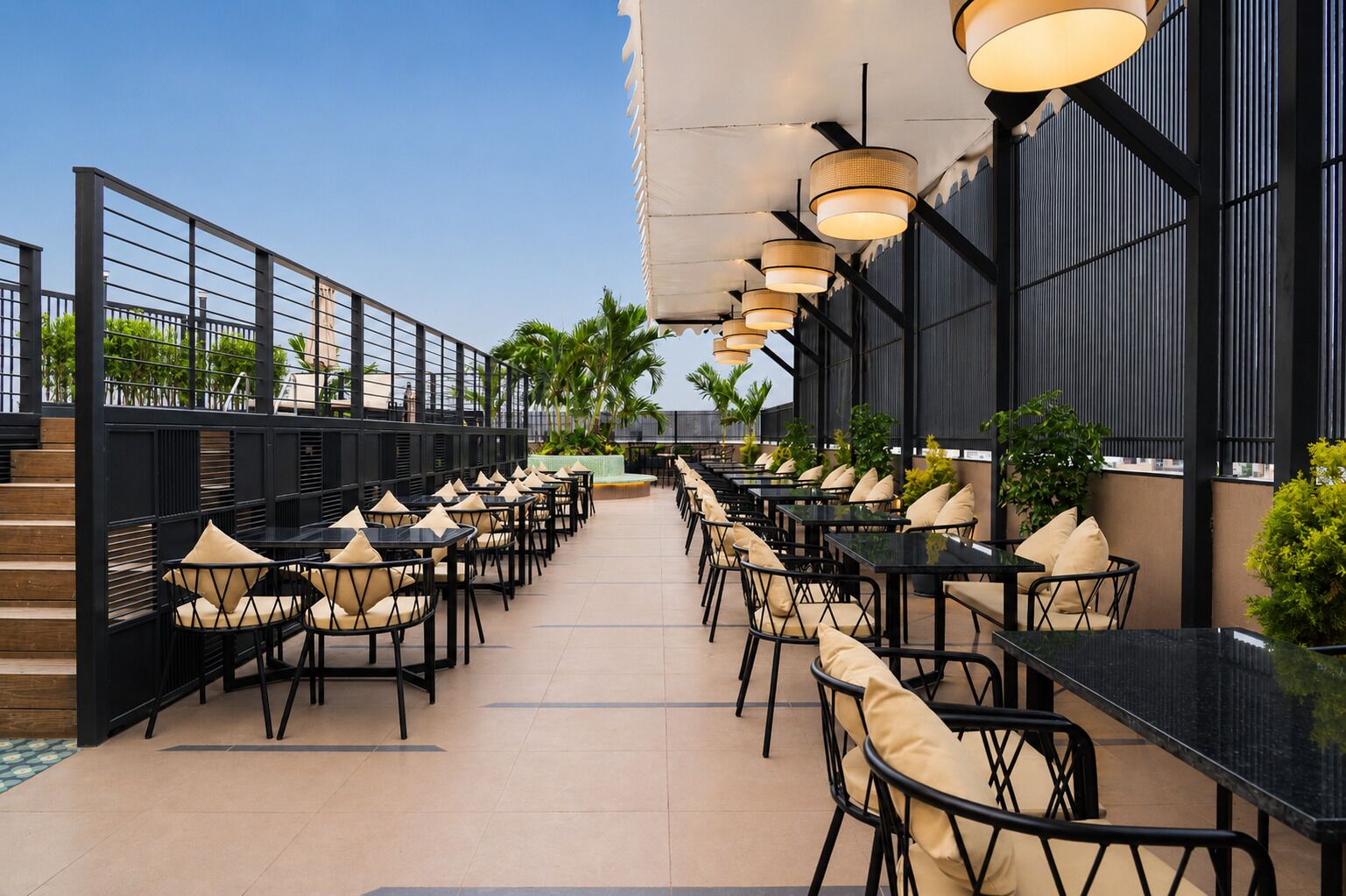 An outdoor dining area with black tables and chairs, a railing on one side, and hanging lights.