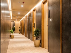 A hallway with multiple elevators, potted plants, and a carpeted floor. - The Avenor - Luxury Hotel in Jaipur (Jaipur)