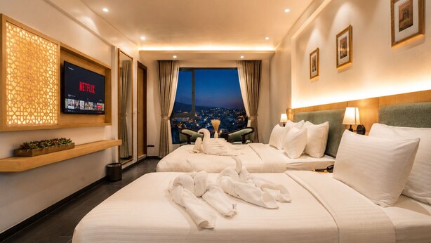 A hotel room with two beds, a TV, a city view, and a wooden shelf with decorative items. - The Avenor - Luxury Hotel in Jaipur (Jaipur)