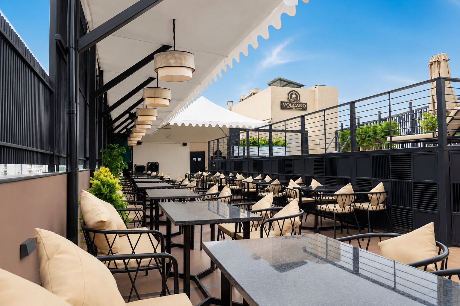 Un espacio de comedor al aire libre con varias mesas y sillas, una sección cubierta y un edificio con un letrero al fondo.