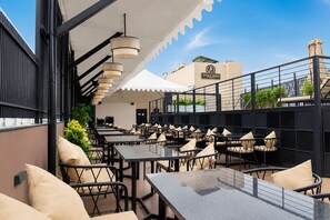 An outdoor dining area with multiple tables and chairs, a covered section, and a building with a sign in the background. - The Avenor - Luxury Hotel in Jaipur (Jaipur)