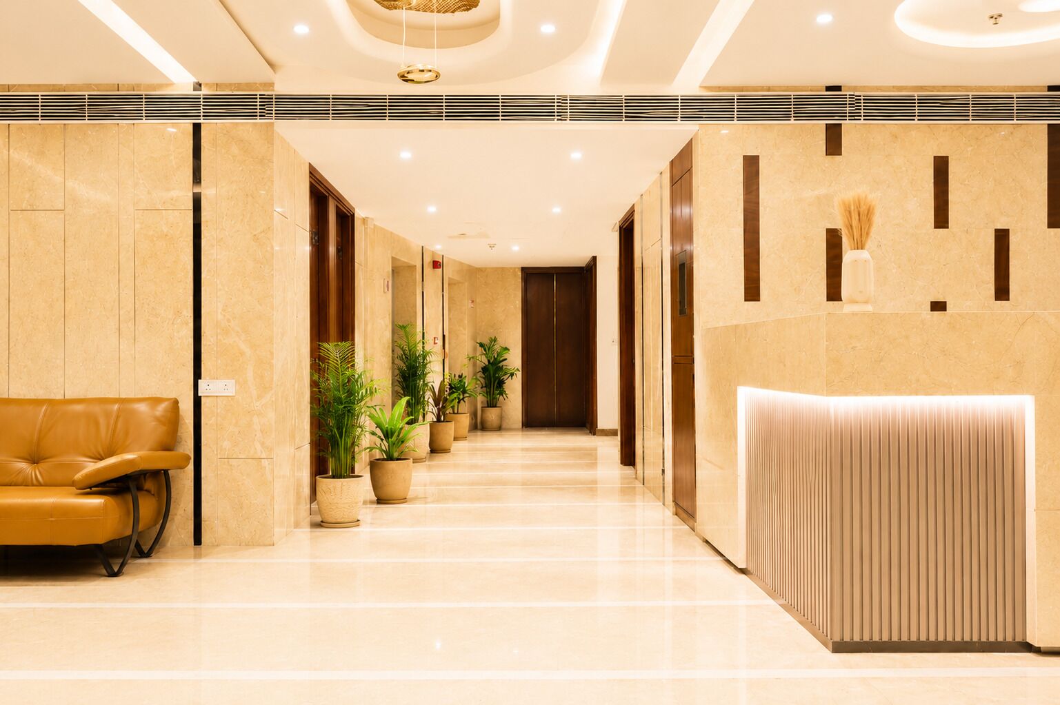 Un vestíbulo de hotel con una mesa de recepción, un sofá de cuero, plantas en macetas y un diseño de techo moderno.