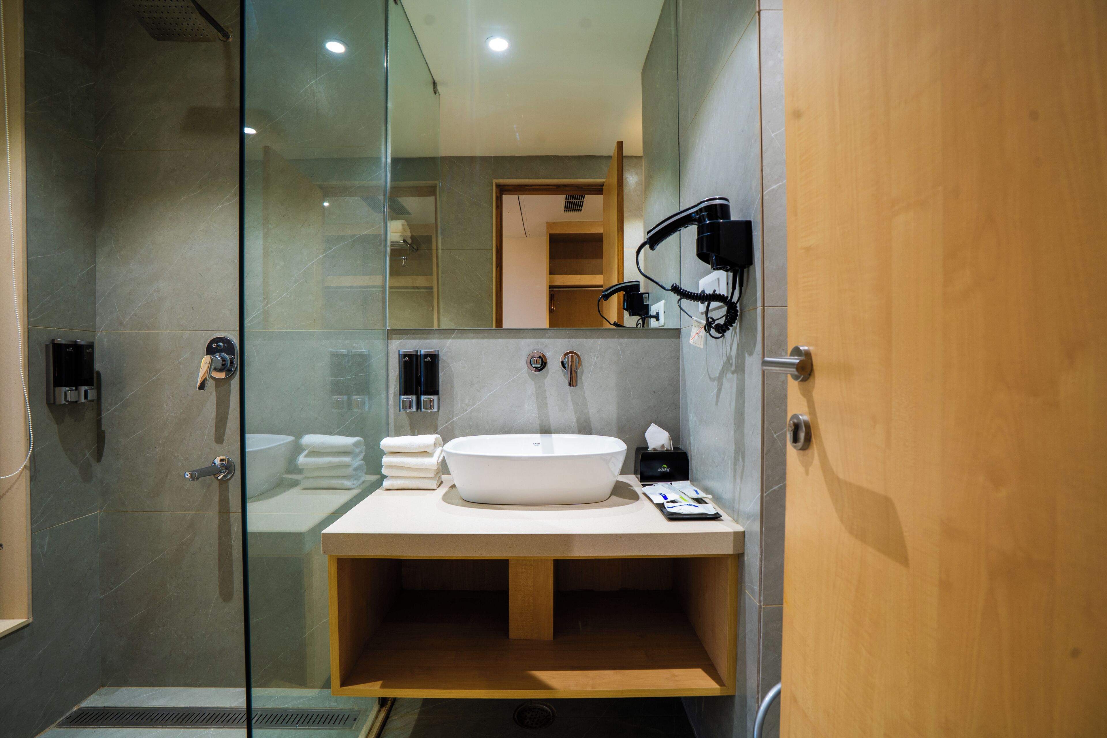 Un baño moderno con cabina de ducha de vidrio, tocador de madera con lavamanos y un secador de pelo fijado en la pared.