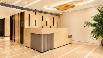 A reception area with a modern design, featuring a reception desk, a potted plant, and a ceiling with recessed lighting.