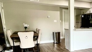 A dining area with a table and chairs, a trash can, and a kitchen area with appliances. - Entire home ,Clean, quiet, and cozy—everything you need for the perfect stay (Virginia Beach)