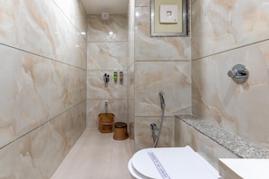 A bathroom with marble walls, a toilet, a shower, and a hand dryer. - Hotel Altura CHHATRAL (Kalol)