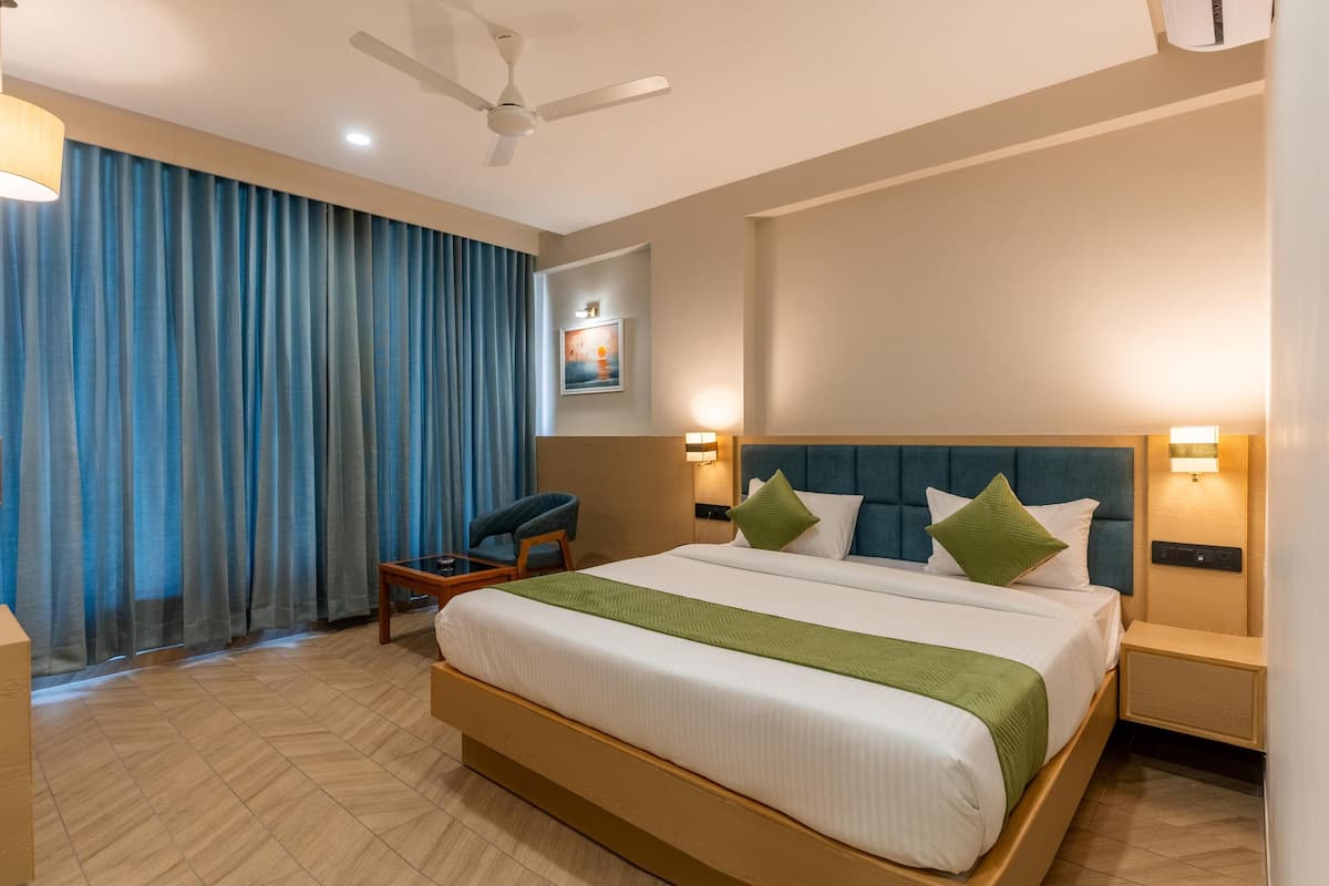 A hotel room with a large bed, a chair, a desk, a ceiling fan, and a wall-mounted light.