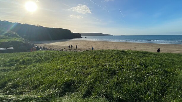 Ein Strand mit einer grünen Rasenfläche im Vordergrund, blauem Himmel und Bergen in der Ferne.