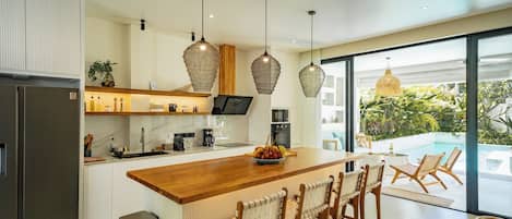 A modern kitchen with a central island, bar stools, pendant lighting, and a view of a pool.