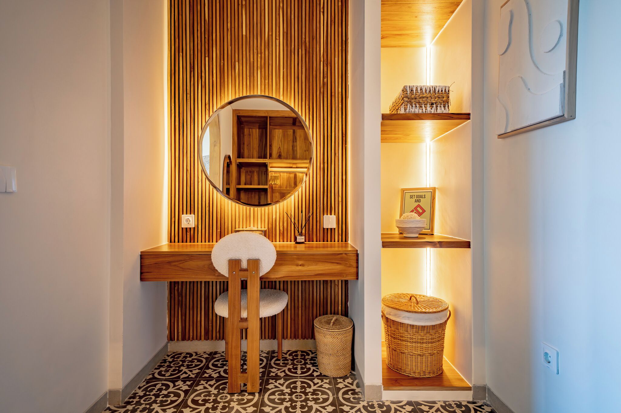 A wooden vanity with a mirror, a chair, and shelves with decorative items.