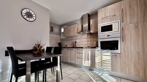 Uma cozinha moderna com armários de madeira clara, forno embutido e um espaço de jantar com mesa e cadeiras escuras.