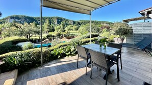 Pátio externo com mesa e cadeiras, rodeado por um deck de madeira e vista para uma paisagem montanhosa.