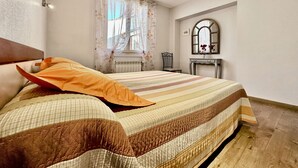 Um quarto com cama, cadeira, penteadeira, espelho e janela com cortinas.