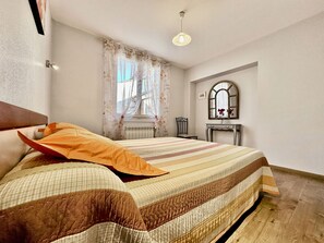 Ein Schlafzimmer mit Bett, Stuhl, Kommode, Spiegel und einem Fenster mit Vorhängen.