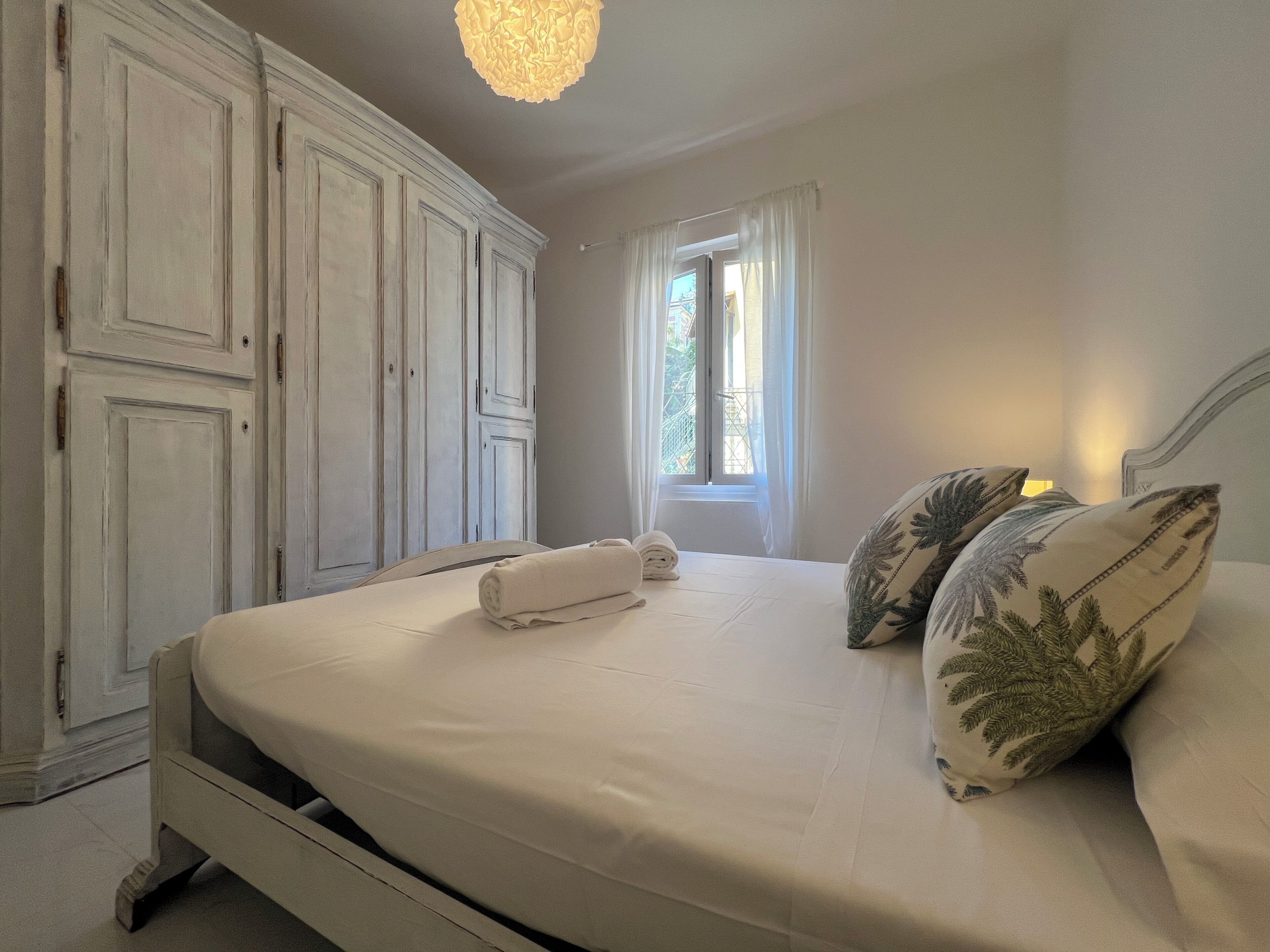 Une chambre à coucher comprenant un lit, une armoire, une fenêtre avec des rideaux et un luminaire suspendu.