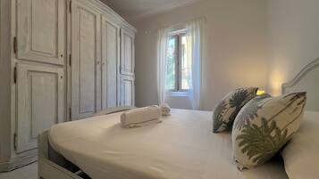 Une chambre à coucher comprenant un lit, une armoire, une fenêtre avec des rideaux et un luminaire suspendu.