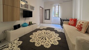 Un salon moderne doté d’un téléviseur à écran plat, d’un canapé agrémenté de coussins décoratifs, d’un tapis à motifs et d’un coin repas avec une table et des chaises.