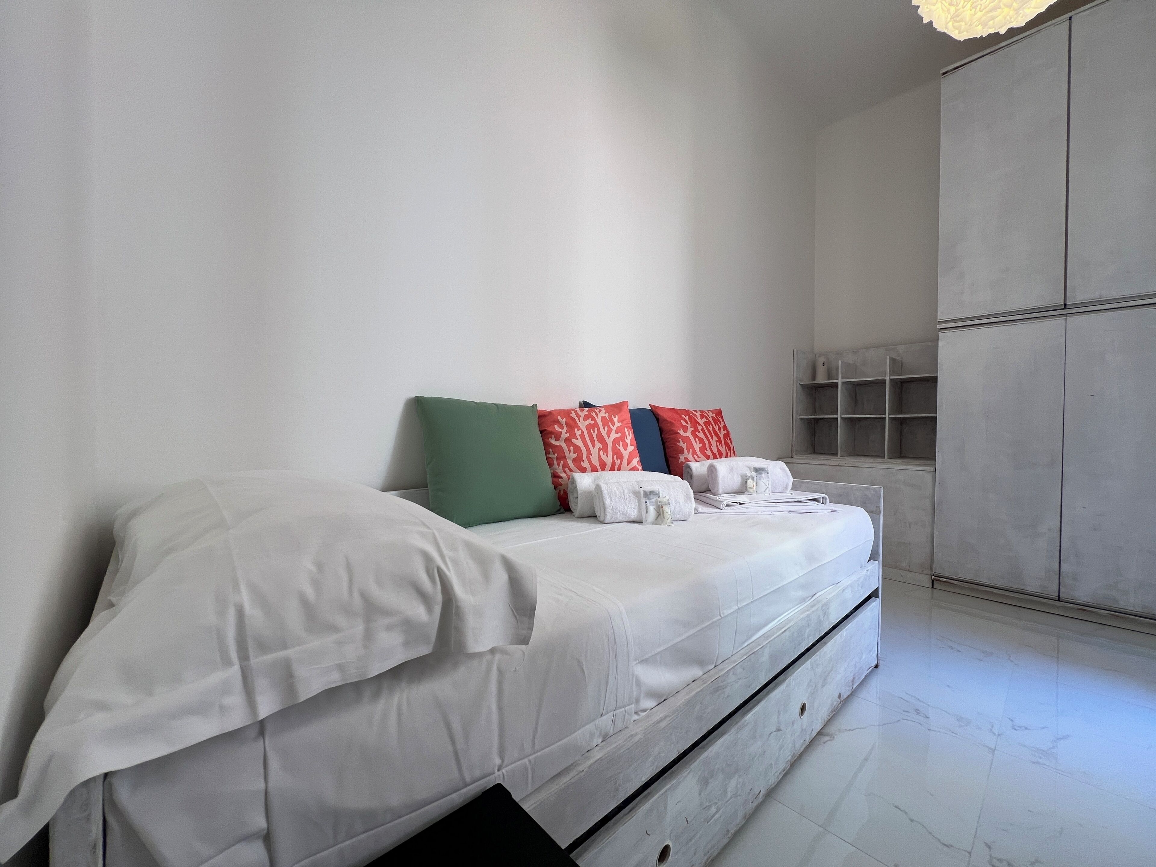 A bed with white bedding, a green pillow, and red patterned pillows.