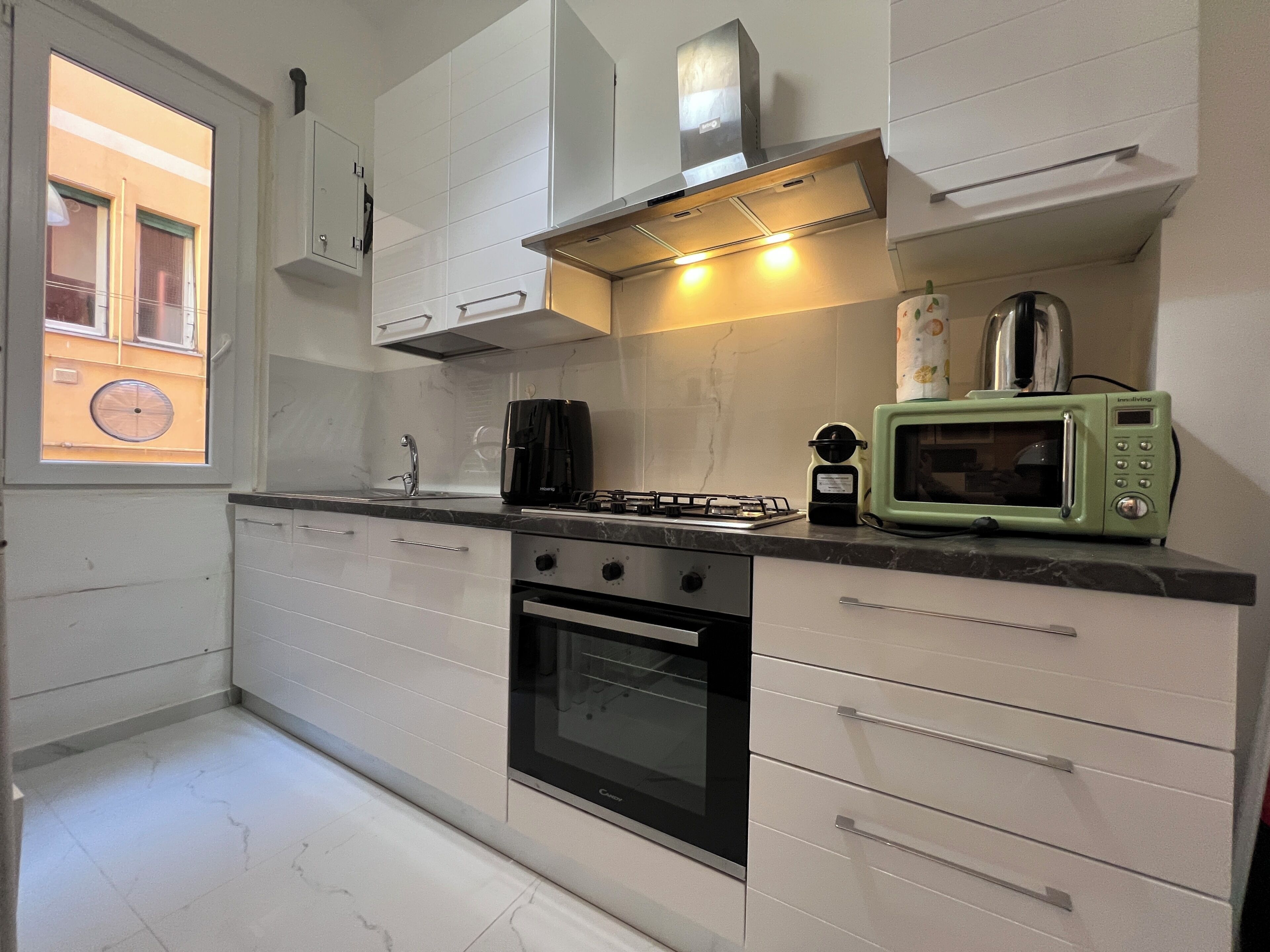 A modern kitchen with white cabinets, a gas stove, a microwave, and a window with a view of a building.