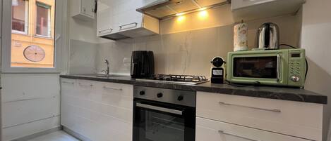 A modern kitchen with white cabinets, a gas stove, a microwave, and a window with a view of a building.