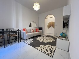 Un soggiorno moderno con un divano, poltrone, un tavolo da pranzo, un tappeto decorativo, una ventola a muro e un lampadario.