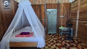 Un lit simple avec un baldaquin, une petite table avec un casque audio, un ventilateur et un sol à motifs.