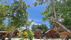 Un complexe hôtelier tropical doté de cabanes en bois, entouré de palmiers et surplombant un ciel d’un bleu limpide.