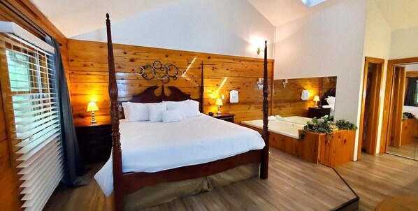 A four-poster bed with a wooden headboard, a bedside table with a lamp, and a small wooden cabinet.
