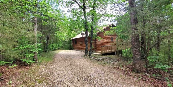 A wooden cabin surrounded by dense forest, with a gravel path leading to it.