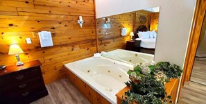 A wooden-paneled room with a large bathtub, a mirror, a wooden dresser, and a plant.