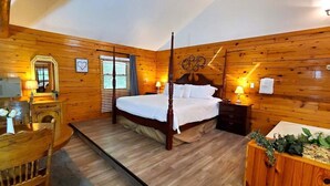 Ein Schlafzimmer mit Holzwandverkleidung, einem Himmelbett, einem Nachttisch, einem Sessel und einem kleinen Tisch mit einer Vase.