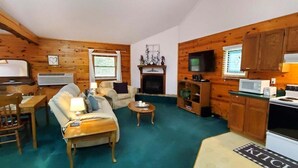 Een knus kamer in chaletstijl met een open haard, houten wanden, een eethoek en een keuken met een fornuis.