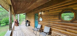 Una cabaña de madera con un porche, una puerta verde y una ventana que da a la vegetación.