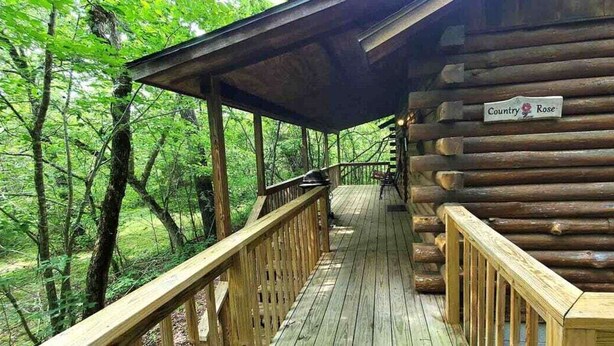 A wooden cabin with a porch, surrounded by trees. - Intimate Log Cabin #2 at Wisteria (Eureka Springs)