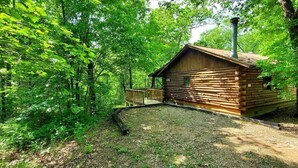 A log cabin with a chimney, surrounded by dense forest. - Intimate Log Cabin #2 at Wisteria (Eureka Springs)