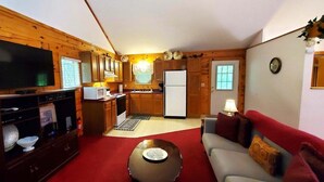 A wooden interior with a TV, kitchen, and a red carpeted area. - Intimate Log Cabin #2 at Wisteria (Eureka Springs)