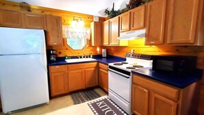 Una cocina compacta con armarios de madera, un refrigerador blanco, una estufa y un microondas.
