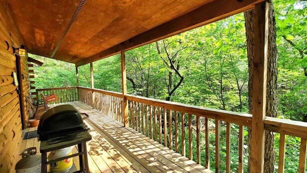 Una terraza de madera con una parrilla, un farol y vistas a un bosque.