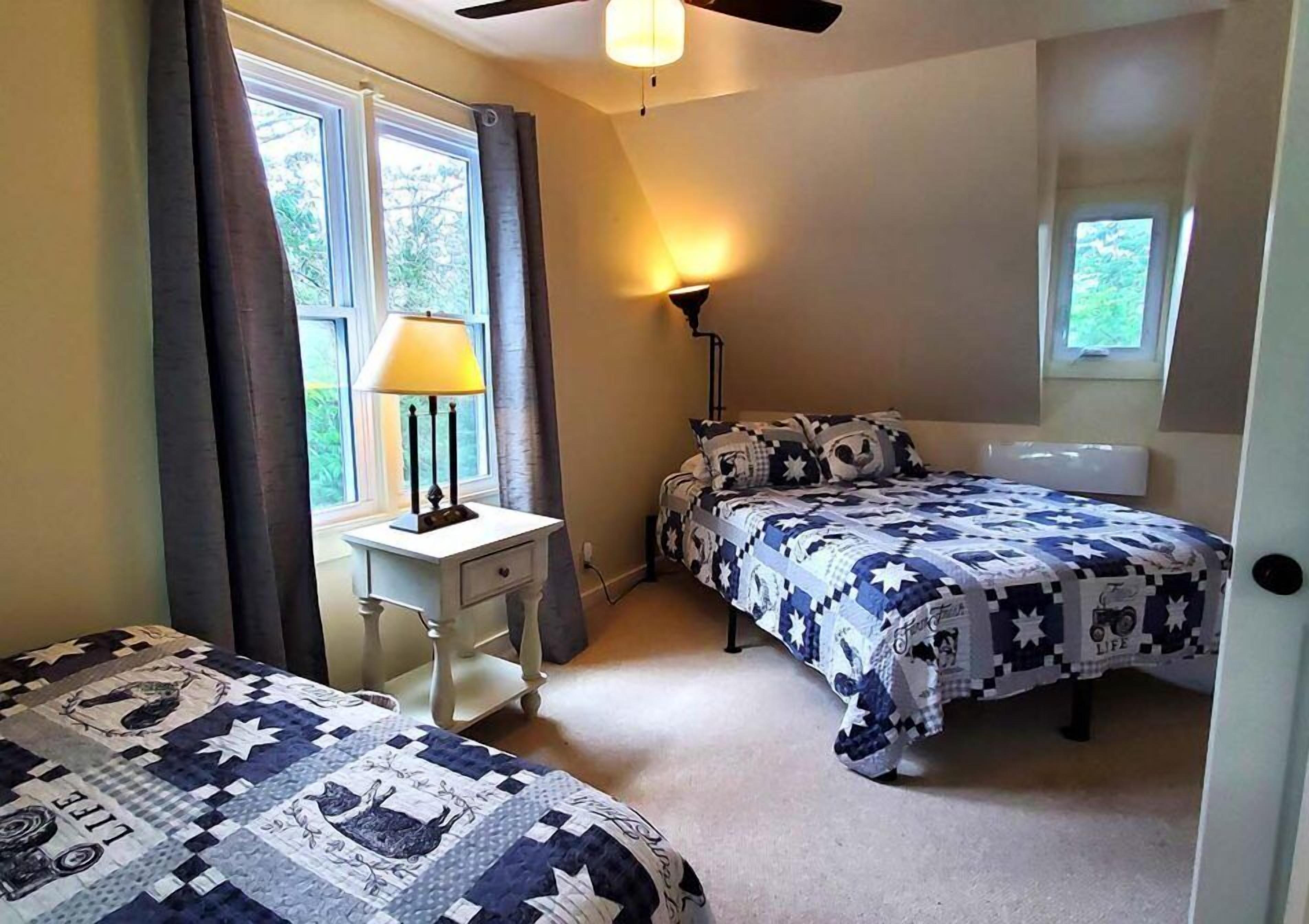 A bedroom with two beds, a desk, a lamp, and a ceiling fan.