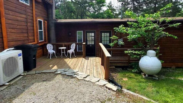 A wooden cabin with a deck, outdoor seating, and a large decorative pot. - Secluded Farm House at Wisteria (Eureka Springs)
