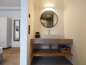 Un baño moderno con un espejo redondo, un lavabo blanco y un estante de madera.